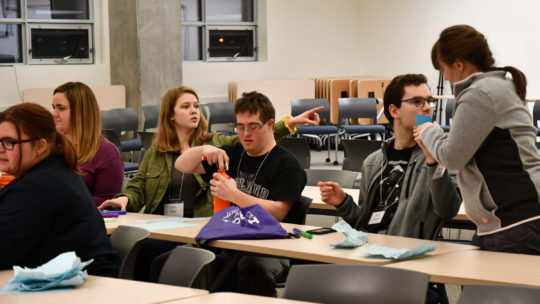 Youth conference attendees work together on a project, a young woman points to where sticky notes can be shared for discussion