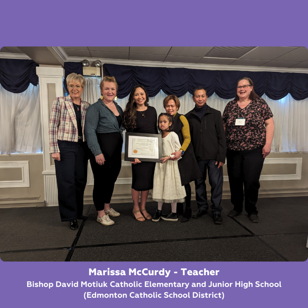 A group of 7 people stand posed toegther on a stage. A person in the middle holds a framed certificate. Below text reads: Marissa McCurdy - Teacher. Bishop David Motiuk Catholic Elementary and Junior High School (Edmonton Catholic School District)